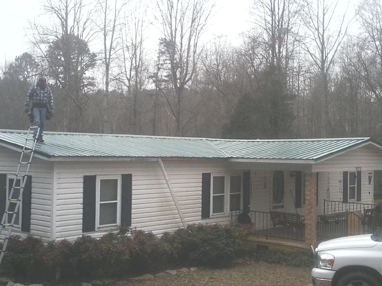 Worker on a ladder beside a new green metal roof on a ranch home in Wallington