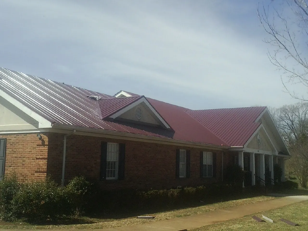 Red metal roof with gabled entries on a long brick building, from a Hail Damage Roof Repair job in Wallington