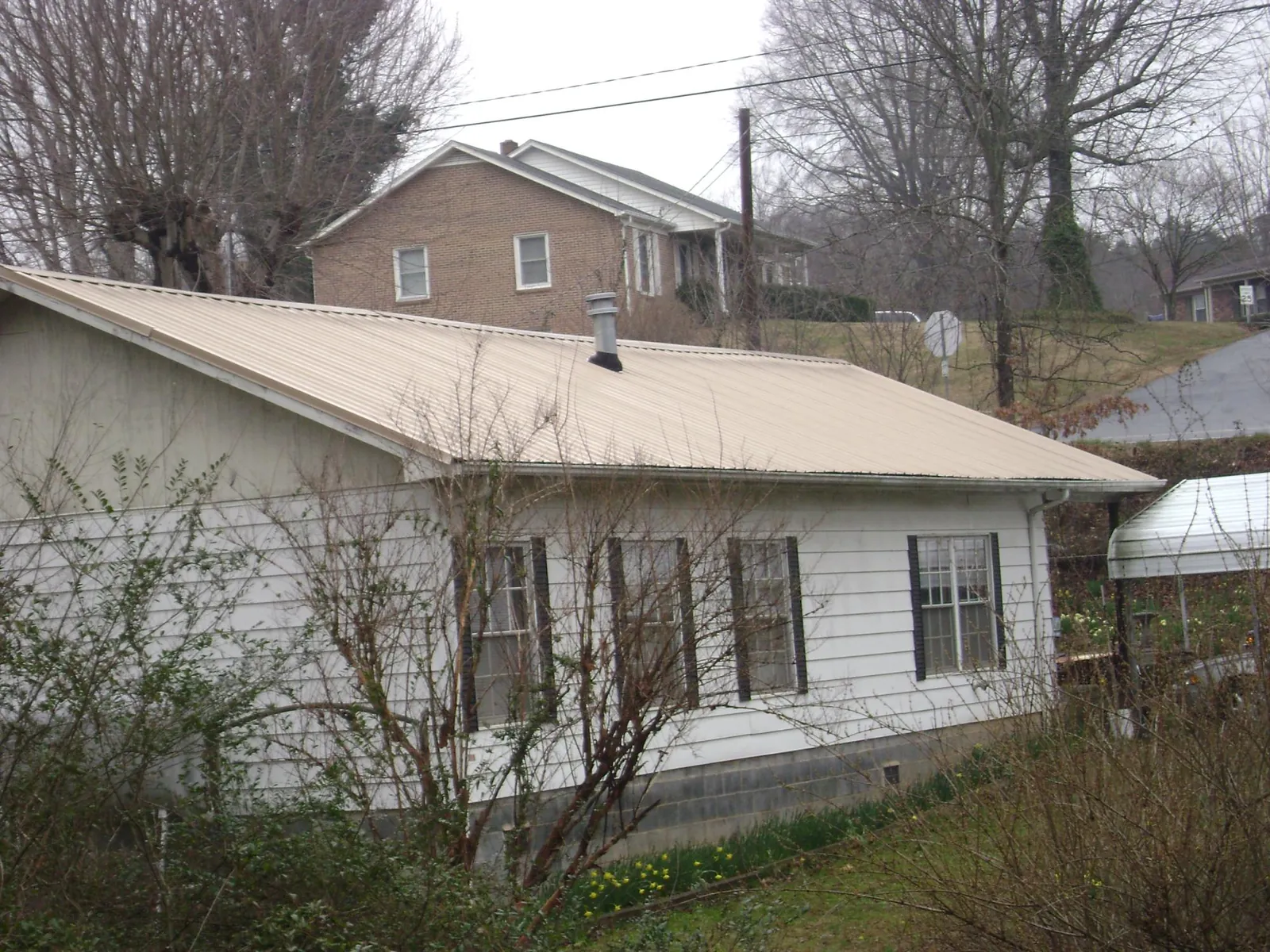 Tan metal roof on a white sided house set into a hillside — Commercial Roofing by Roofing Brothers in Wallington